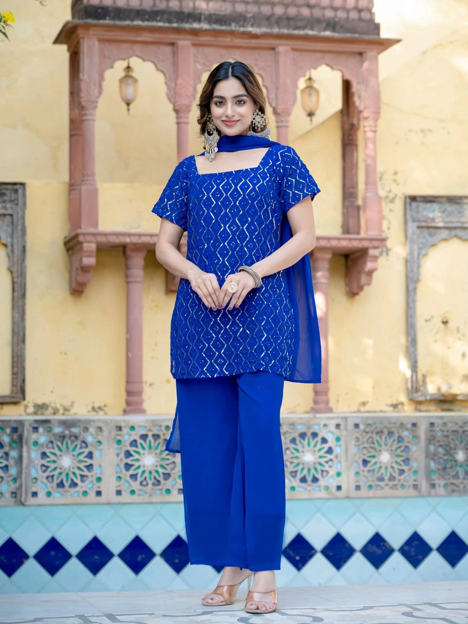 Woman in a blue traditional outfit standing in front of decorative architecture.