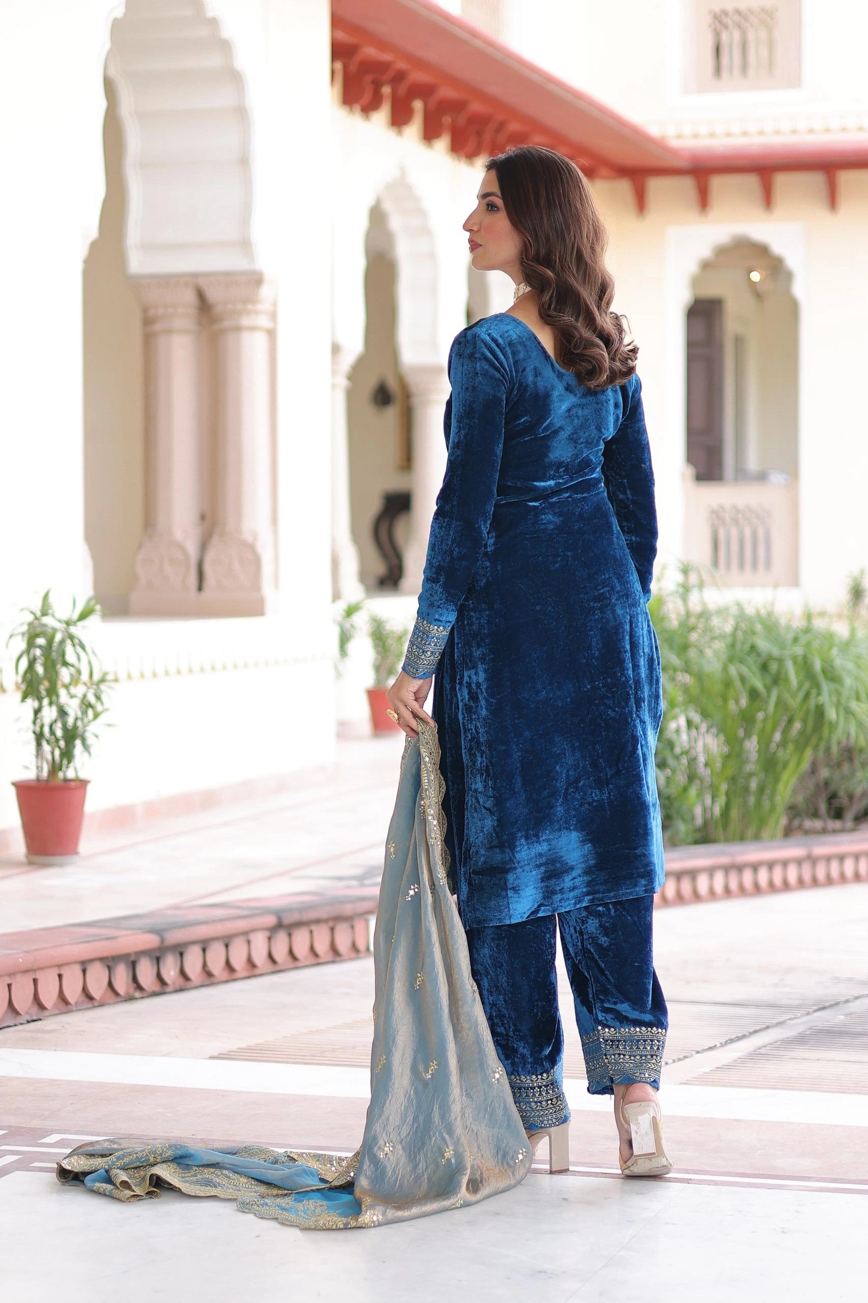 Woman in a blue traditional outfit standing in front of a building with architectural elements.