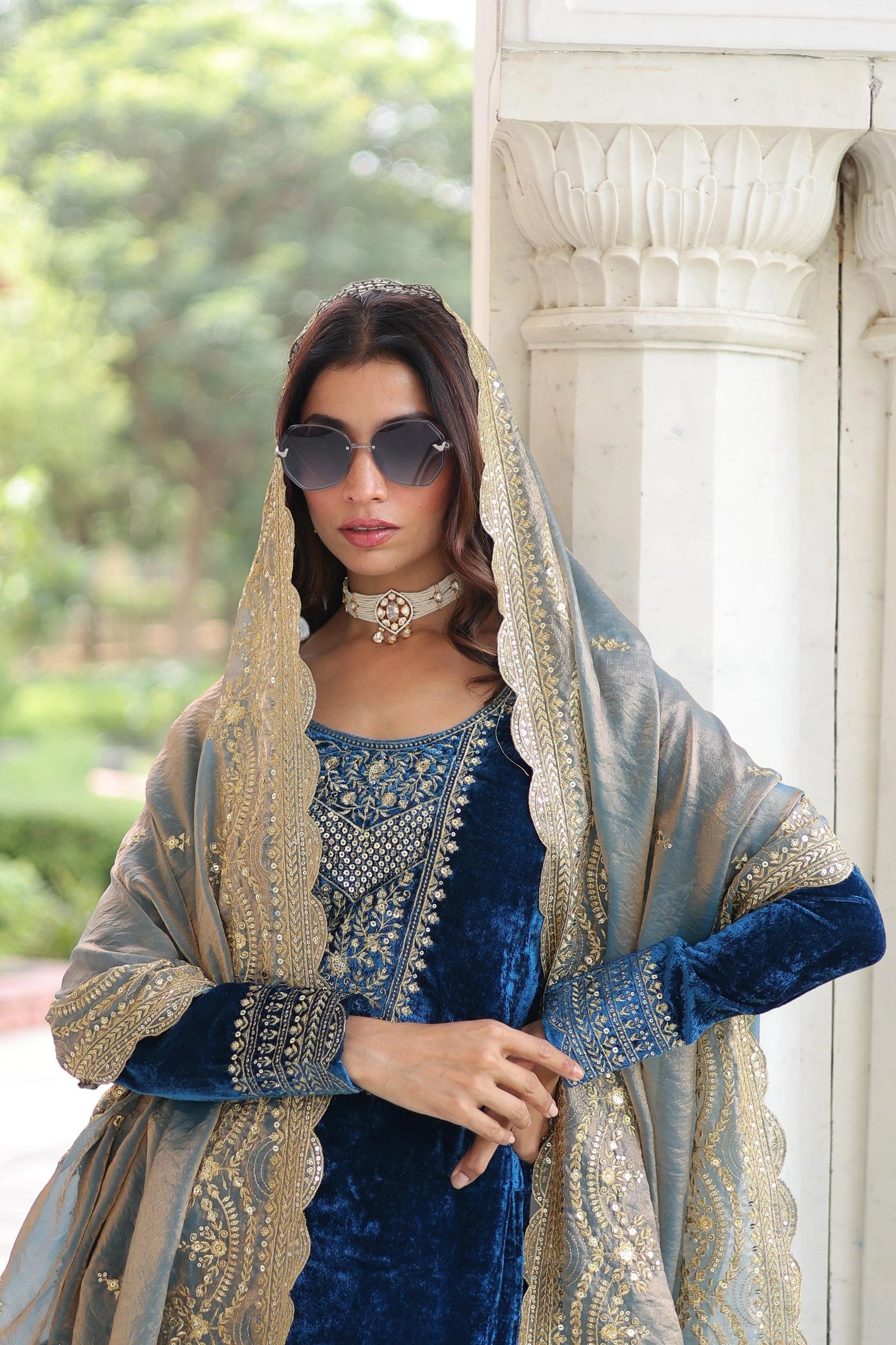 Woman in traditional blue and gold outfit with sunglasses, standing outdoors.