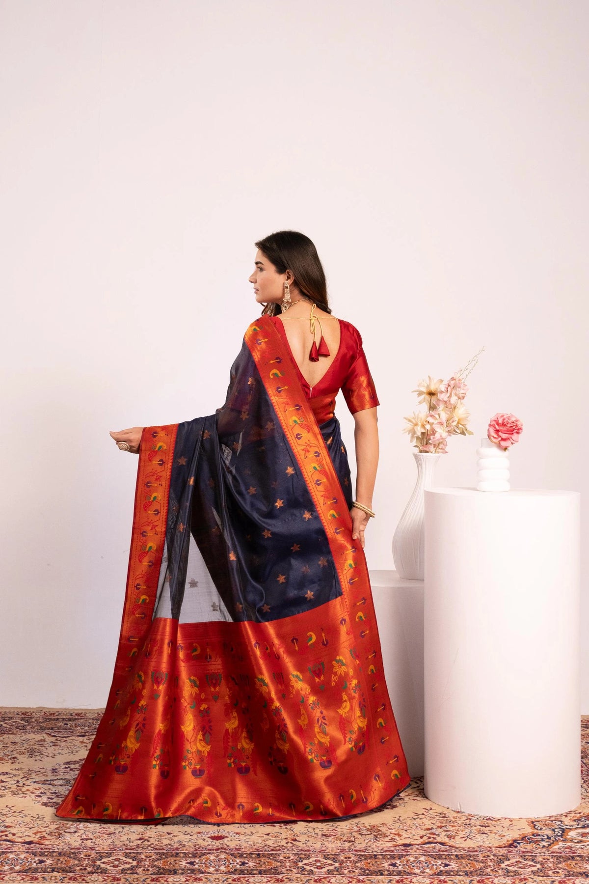 Woman wearing a traditional saree with a red and blue pattern, standing against a plain background.