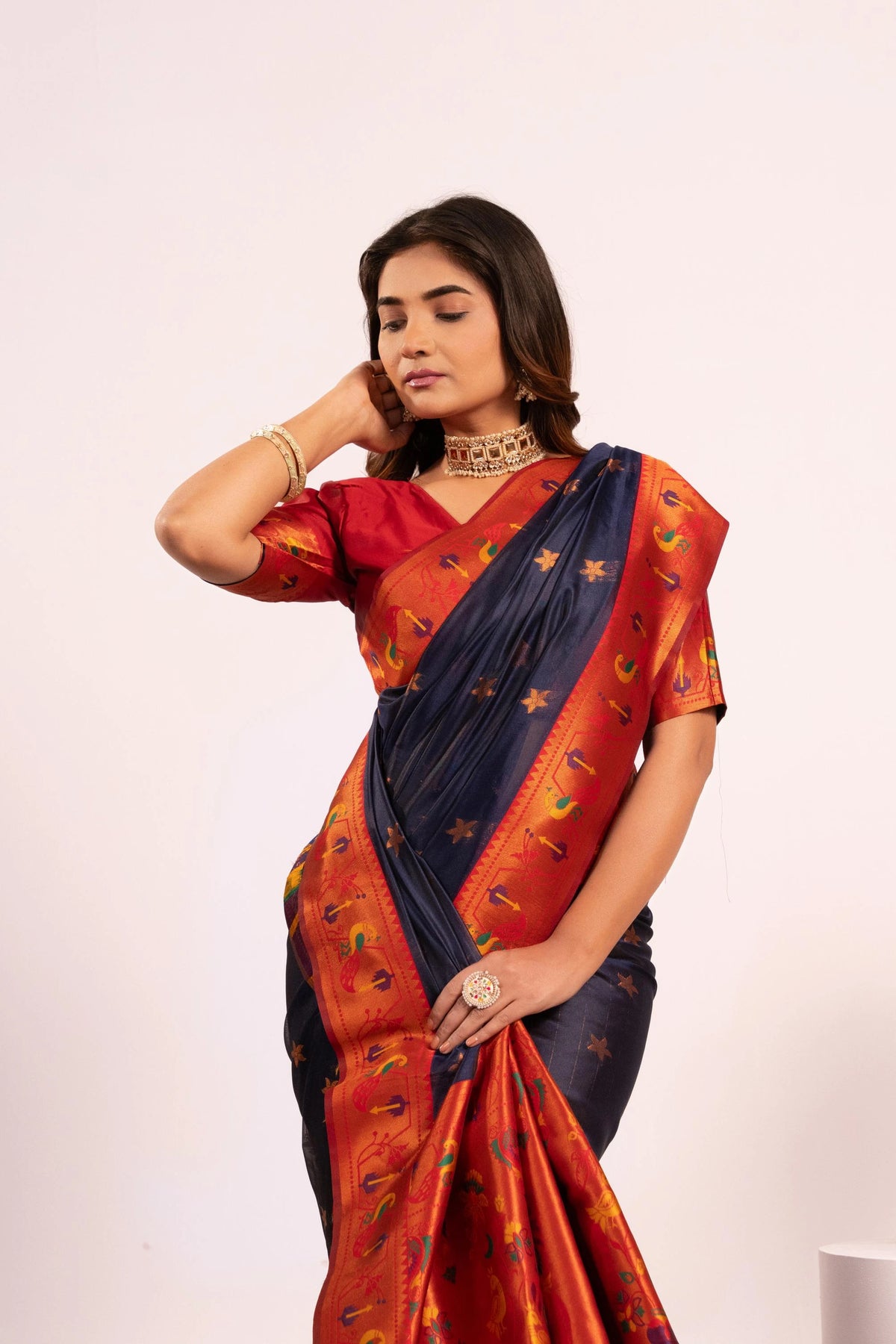 Woman wearing a traditional saree with a red and blue pattern on a plain background
