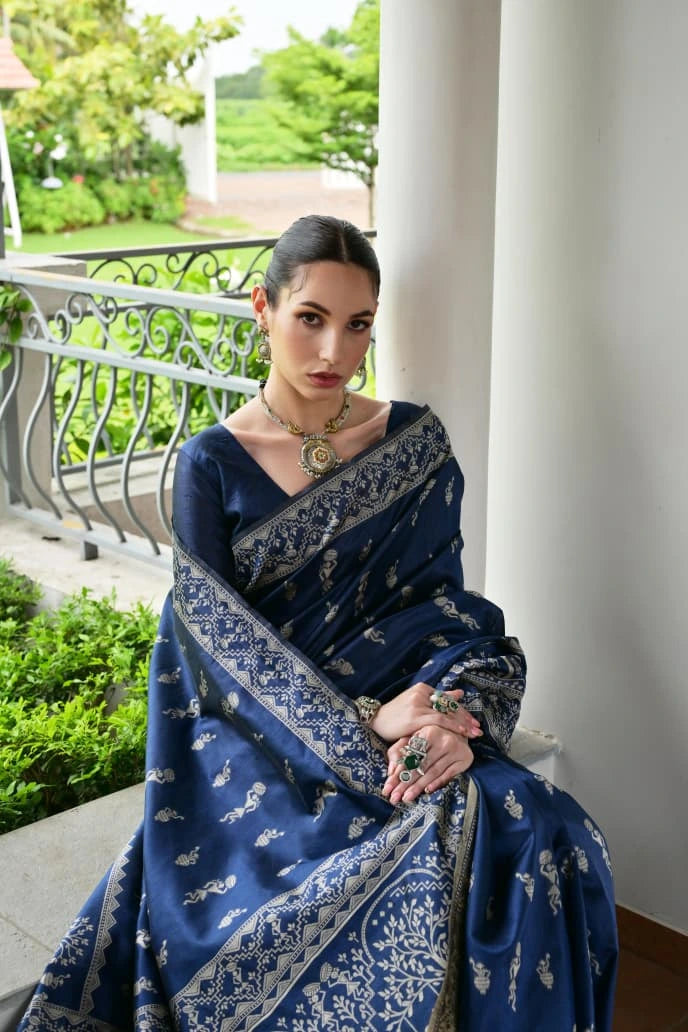 Woman in a blue saree with white patterns sitting on a balcony.