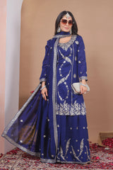 Woman in a blue embroidered traditional outfit with silver details against a beige wall.