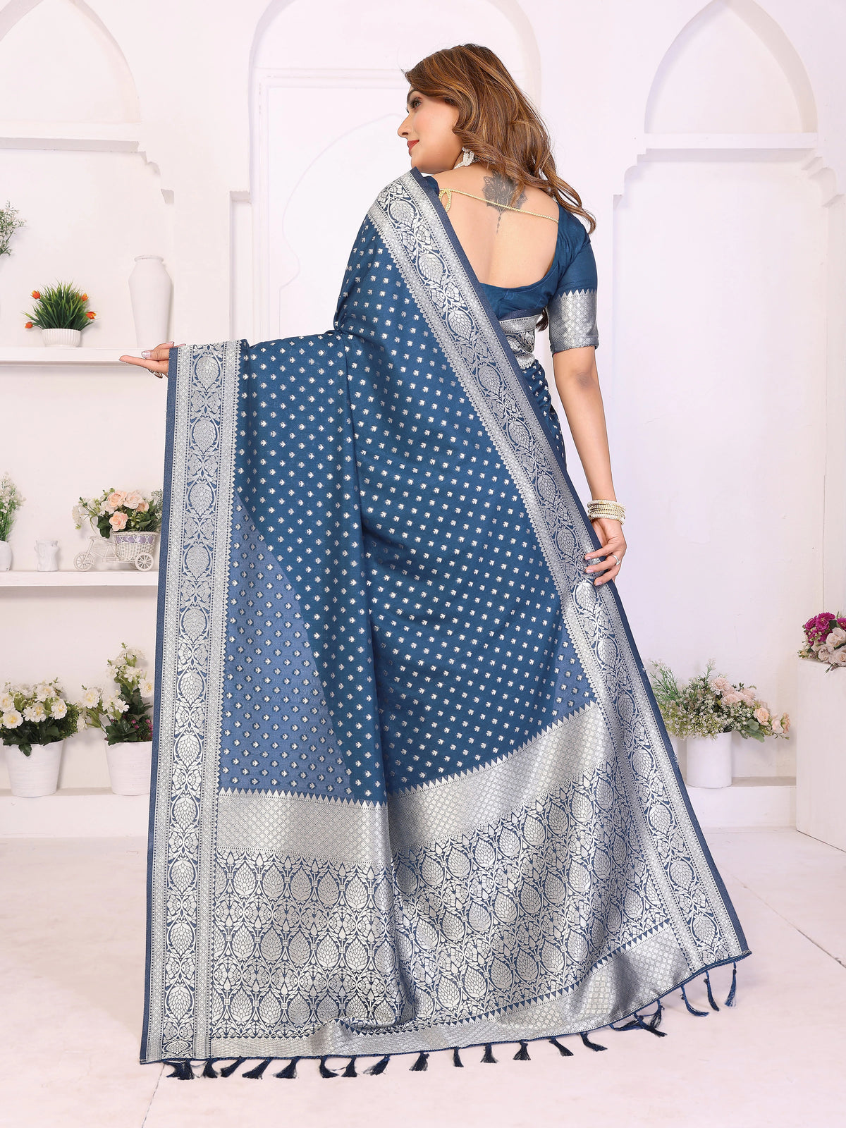 Woman wearing a blue saree with white patterns in a white room.
