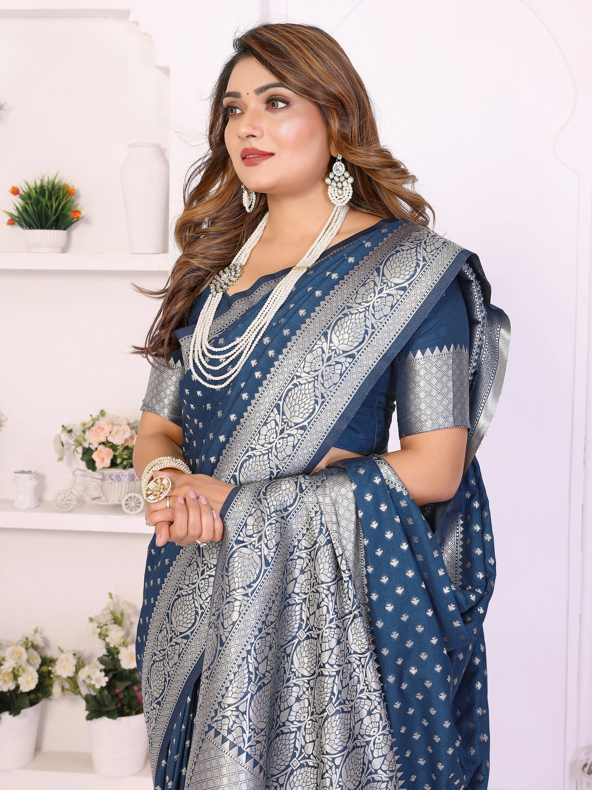 Woman wearing a blue saree with white patterns in a decorative setting.