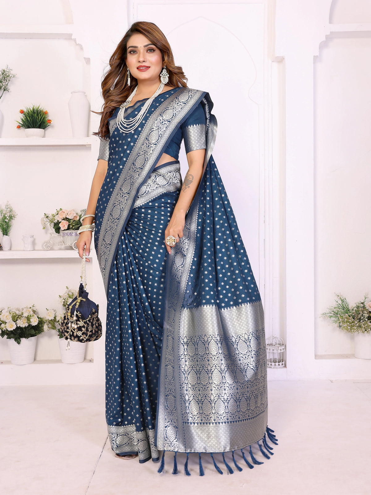 Woman wearing a blue saree with white patterns in a minimalistic room.
