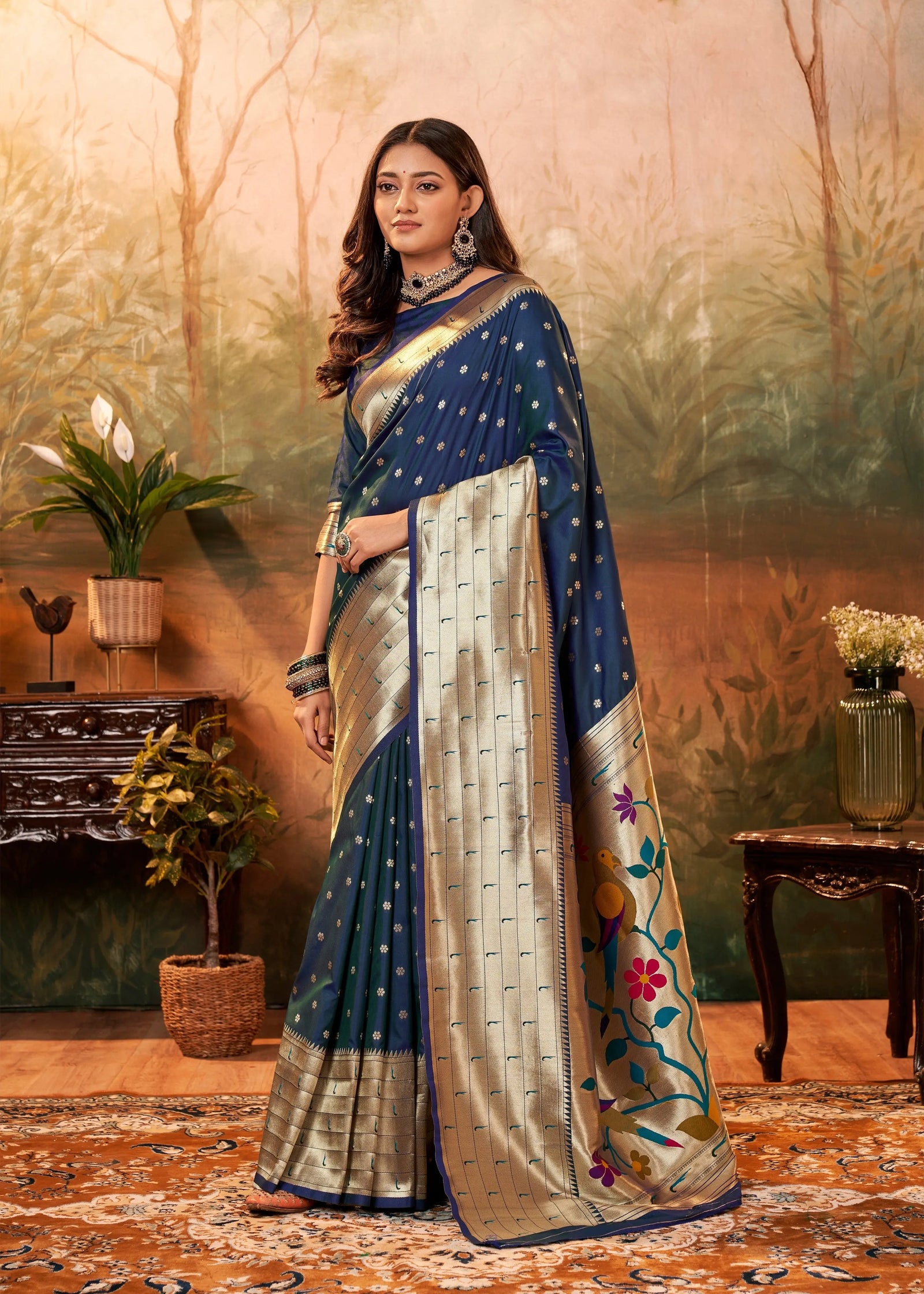 Woman in a traditional saree standing in a decorated room with plants and furniture.
