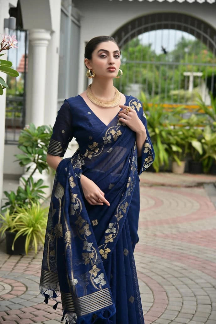 Woman in a blue saree with floral patterns standing outdoors.