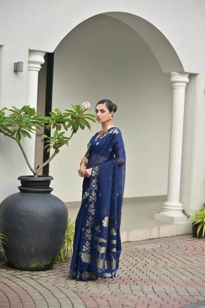 Woman in a blue saree standing in front of a white archway with plants.