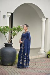 Woman in a blue saree standing in front of a white archway with plants.