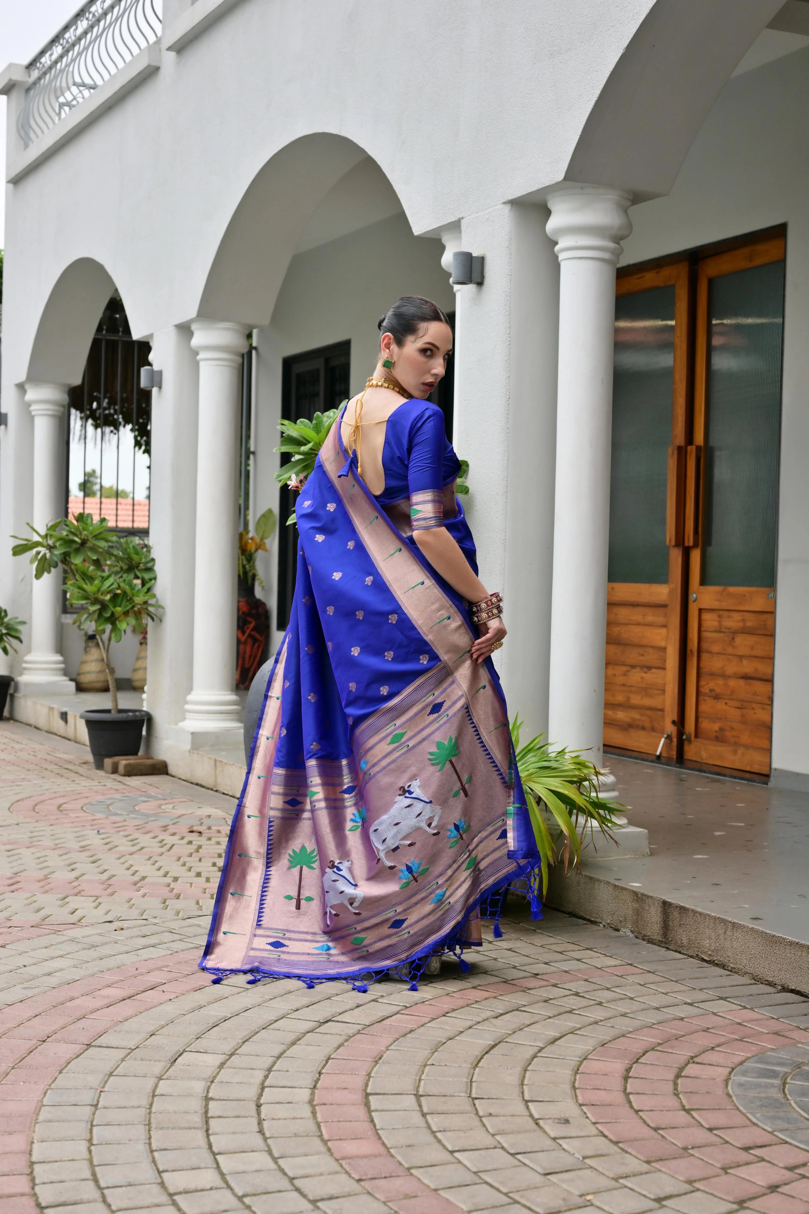 Woman in a blue and pink saree standing in front of a white building with columns.