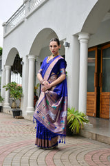 Woman in a blue saree with a patterned border standing in front of a white building.