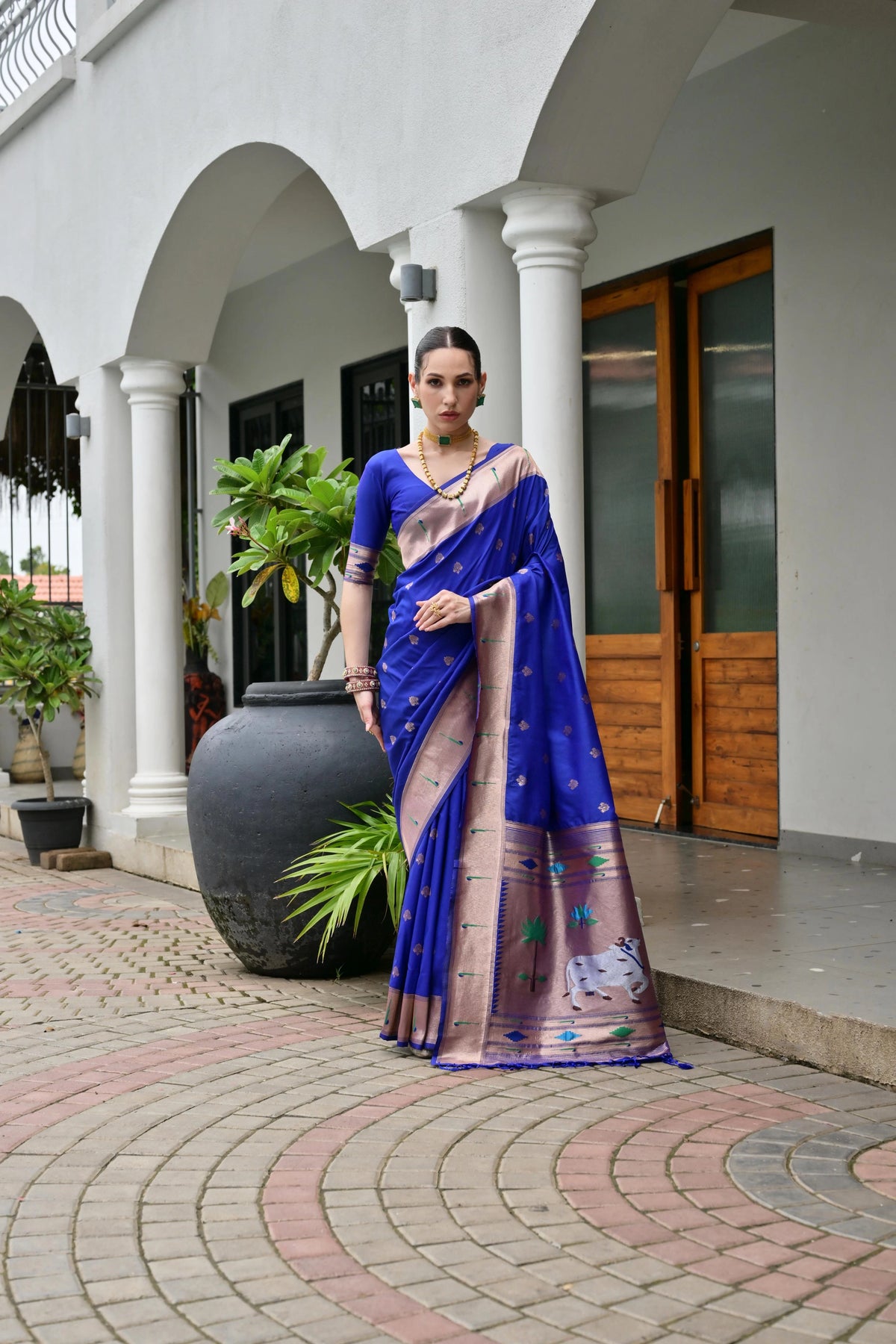 Woman in a blue saree standing outdoors on a paved area.