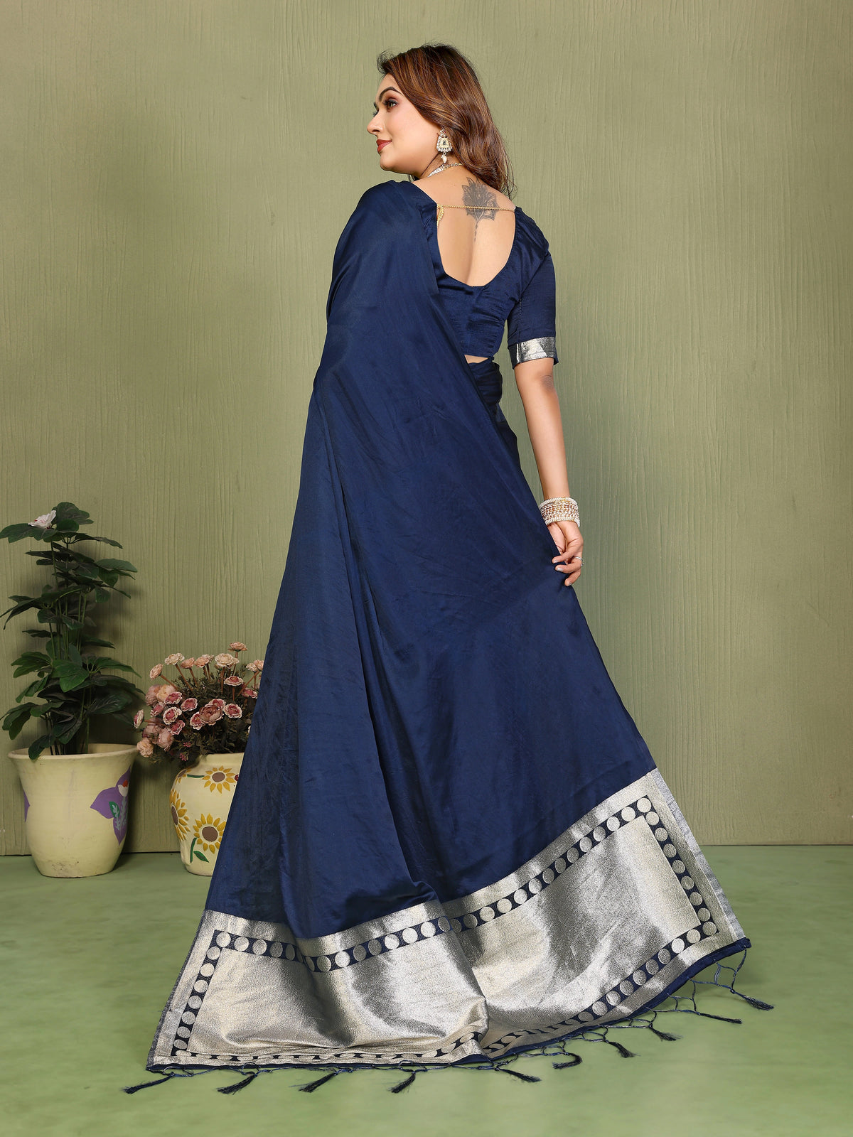 Woman wearing a blue saree with silver border against a green background