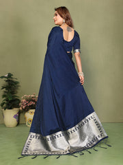 Woman wearing a blue saree with silver border against a green background