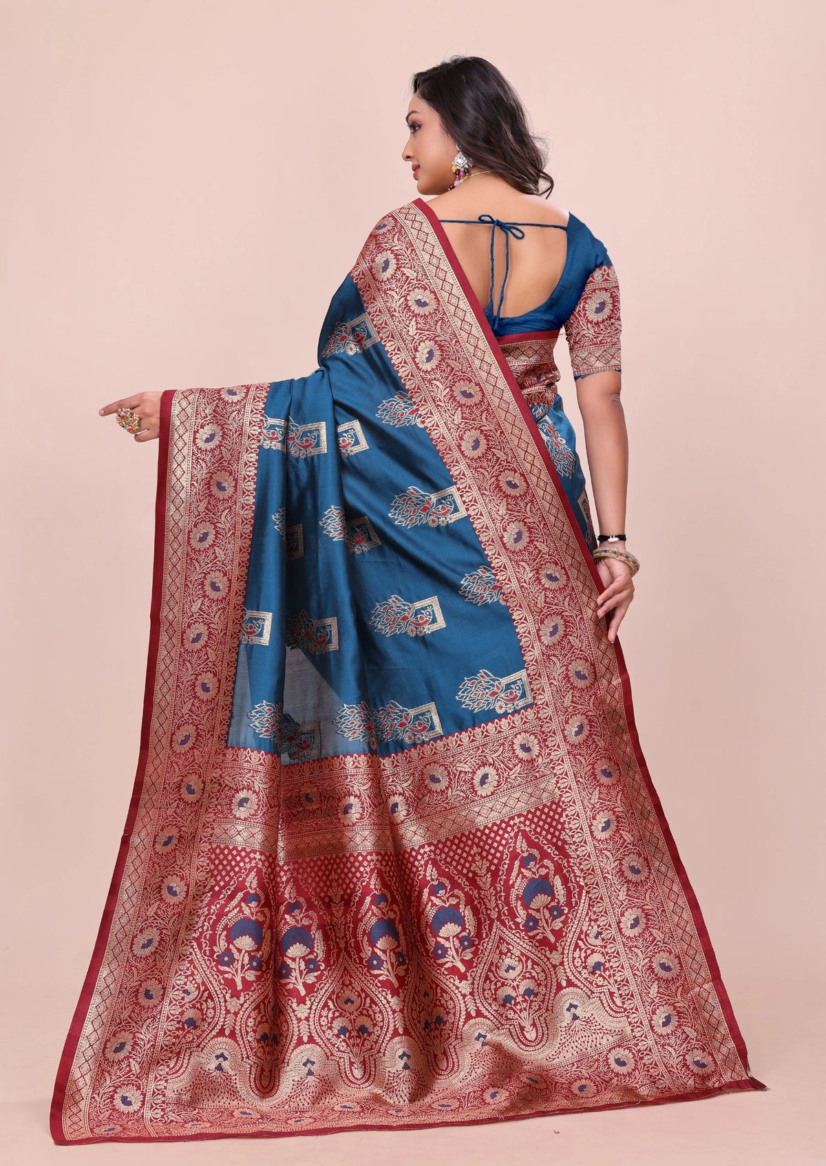 Woman wearing a blue and red saree with intricate patterns on a beige background
