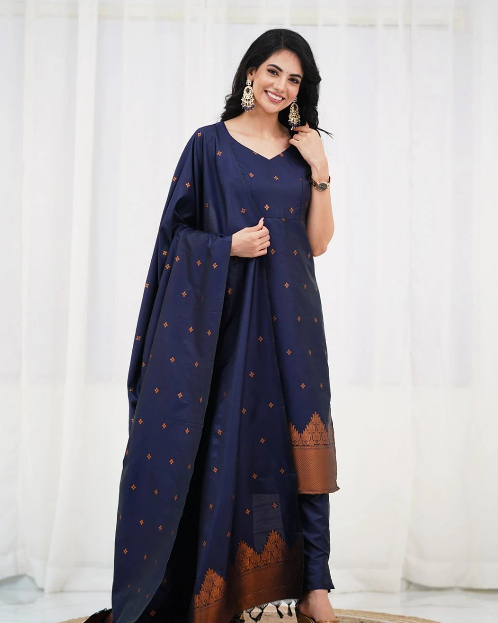 Woman wearing a navy blue traditional outfit with brown patterns against a white curtain background