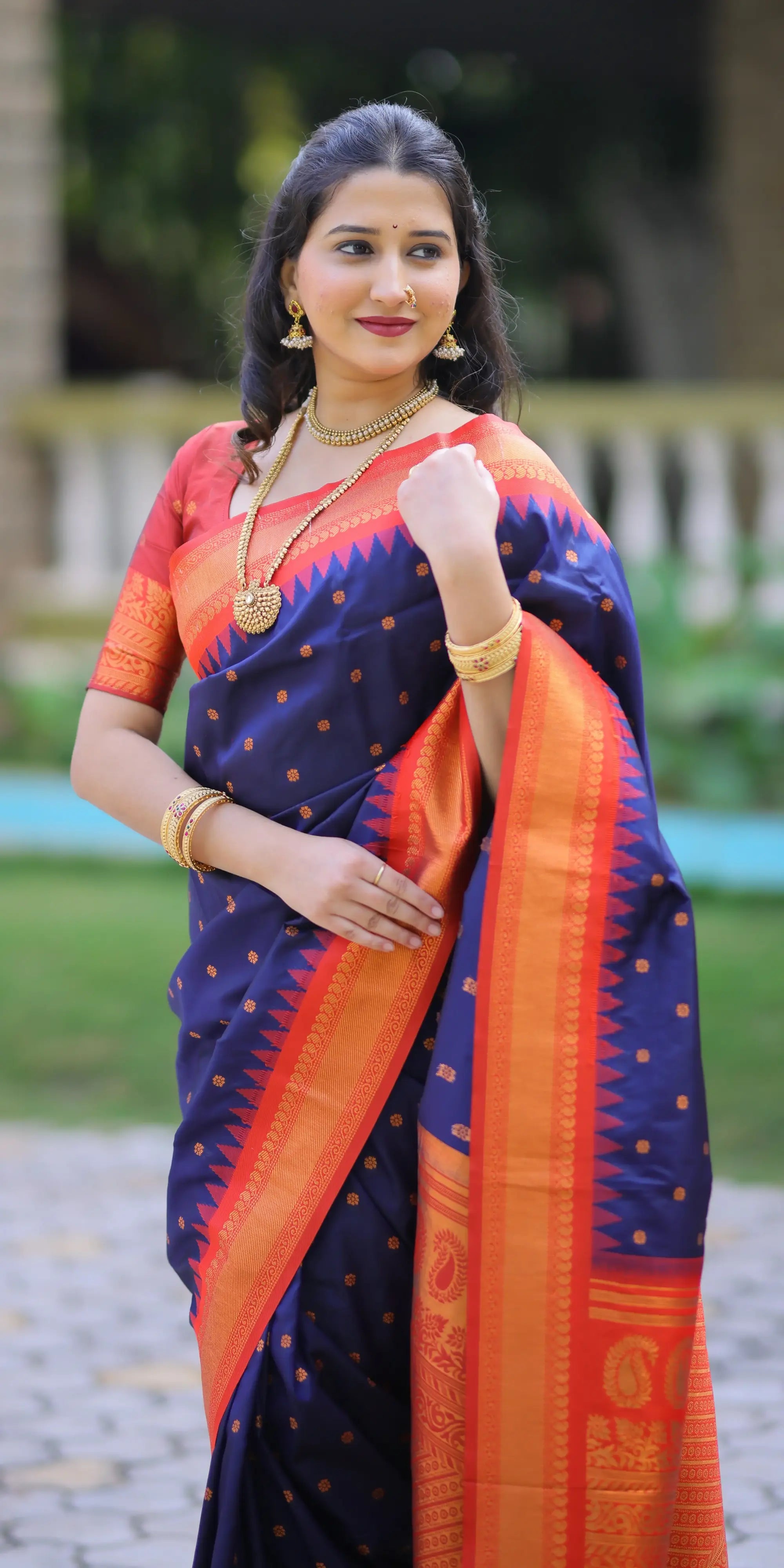 Woman wearing a blue and orange saree with gold jewelry outdoors.