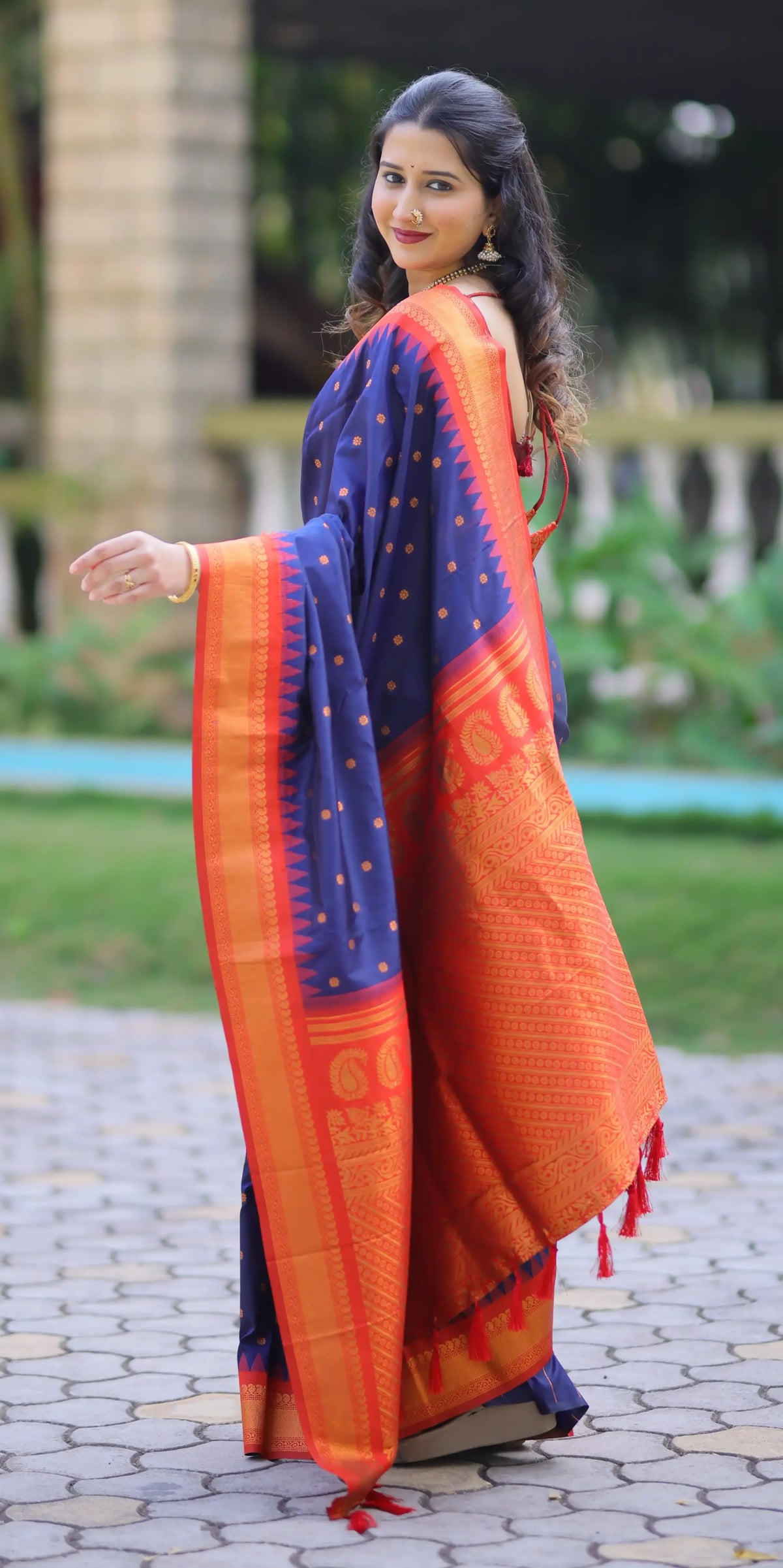Woman wearing an orange and blue saree outdoors on a paved path.