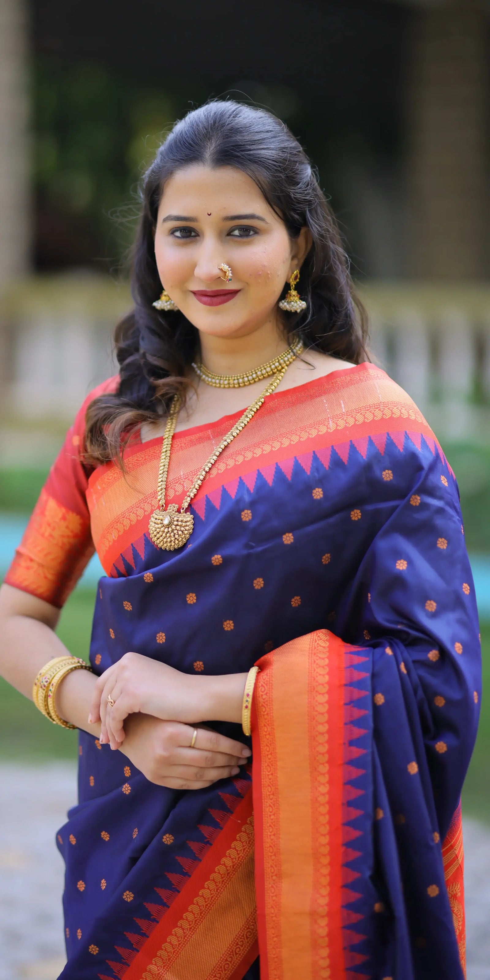Woman wearing a traditional blue and orange saree with jewelry outdoors.