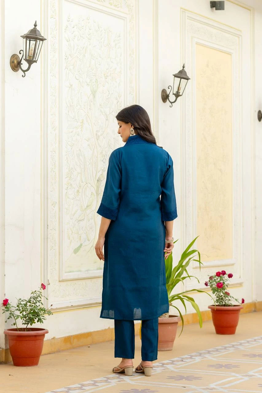 Woman in a blue kurta standing in a decorated room with plants and wall lights.