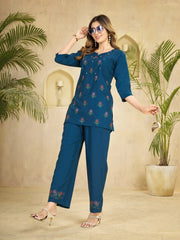 Woman wearing a blue embroidered outfit with plants in the background