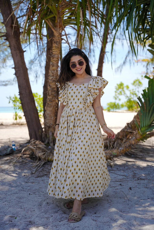 Woman in a patterned dress standing under a palm tree on a beach.