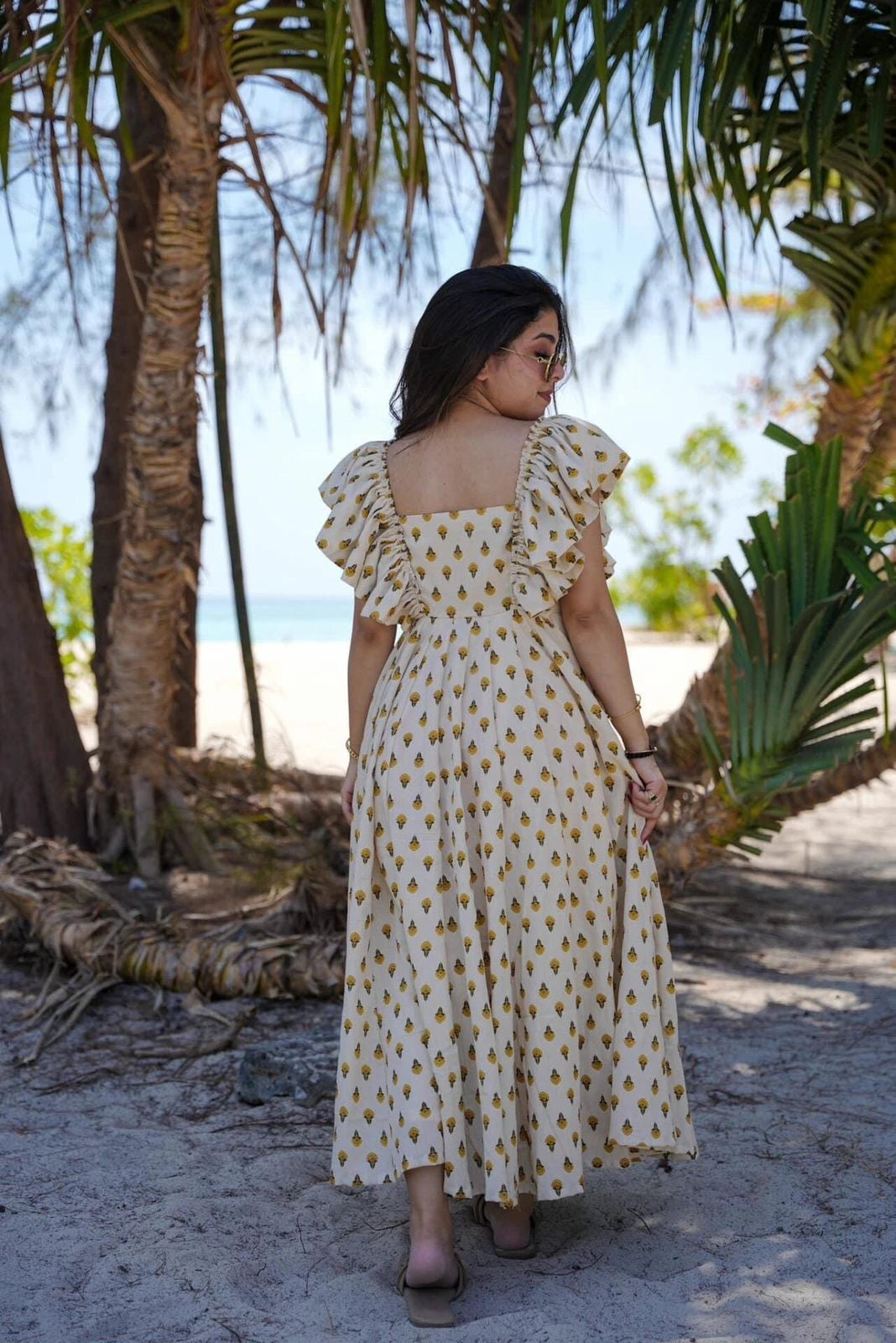 Woman in a polka dot dress standing in a tropical setting with palm trees.