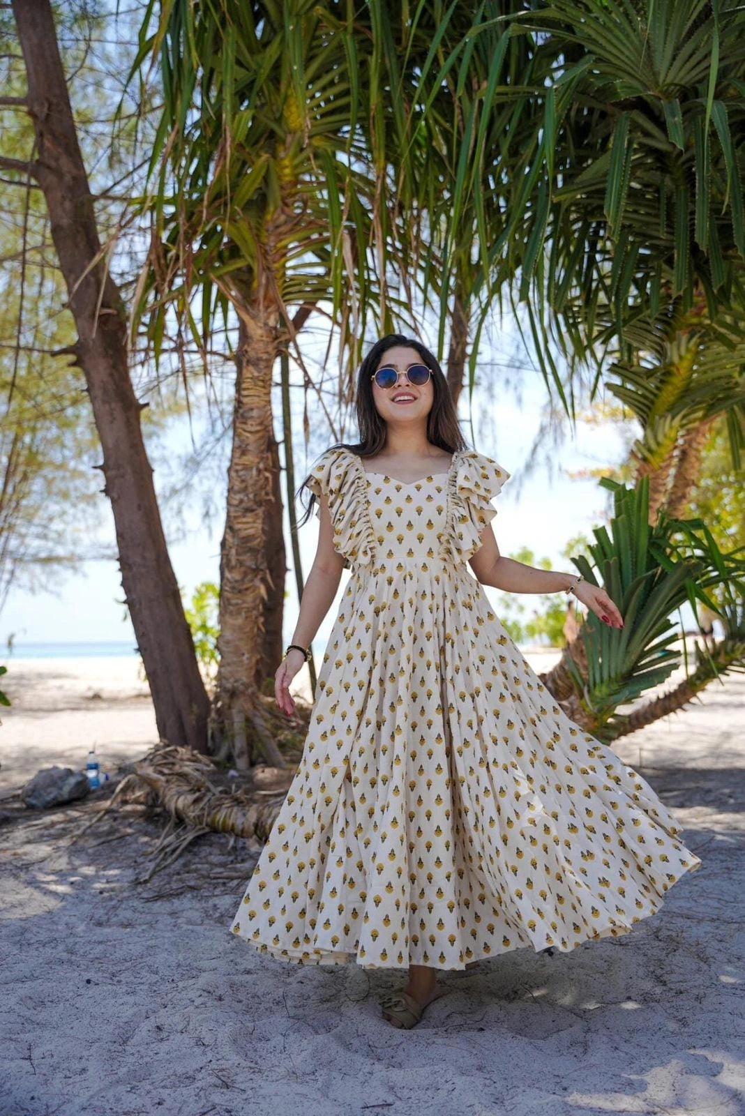 Woman in a patterned dress standing under palm trees on a beach.