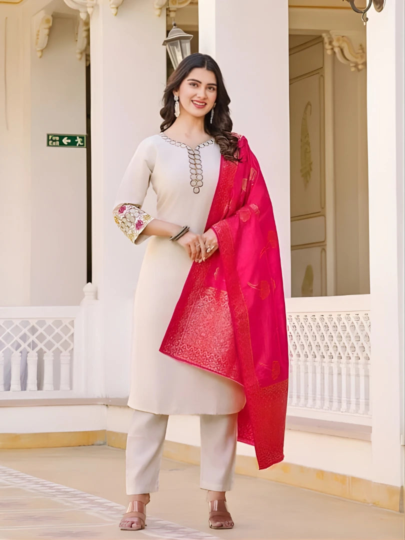 Woman in a white kurta with a red dupatta standing in an elegant indoor setting.