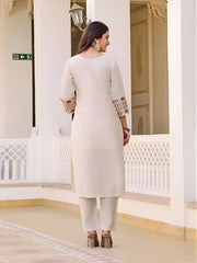 Woman in a white traditional outfit with embroidered sleeves standing in a decorative interior setting.