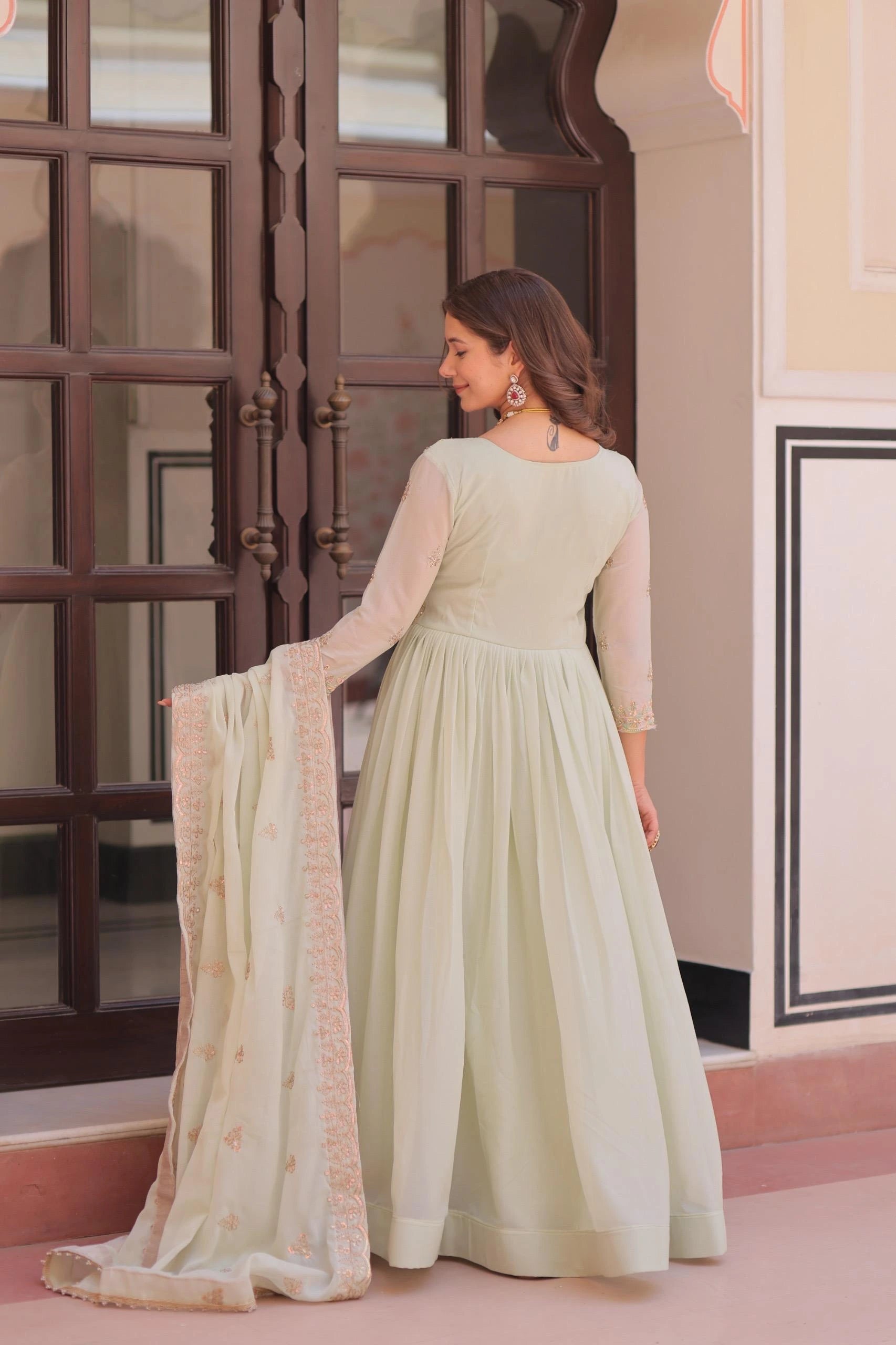 Woman in a light green dress holding a matching dupatta in front of a decorative door.