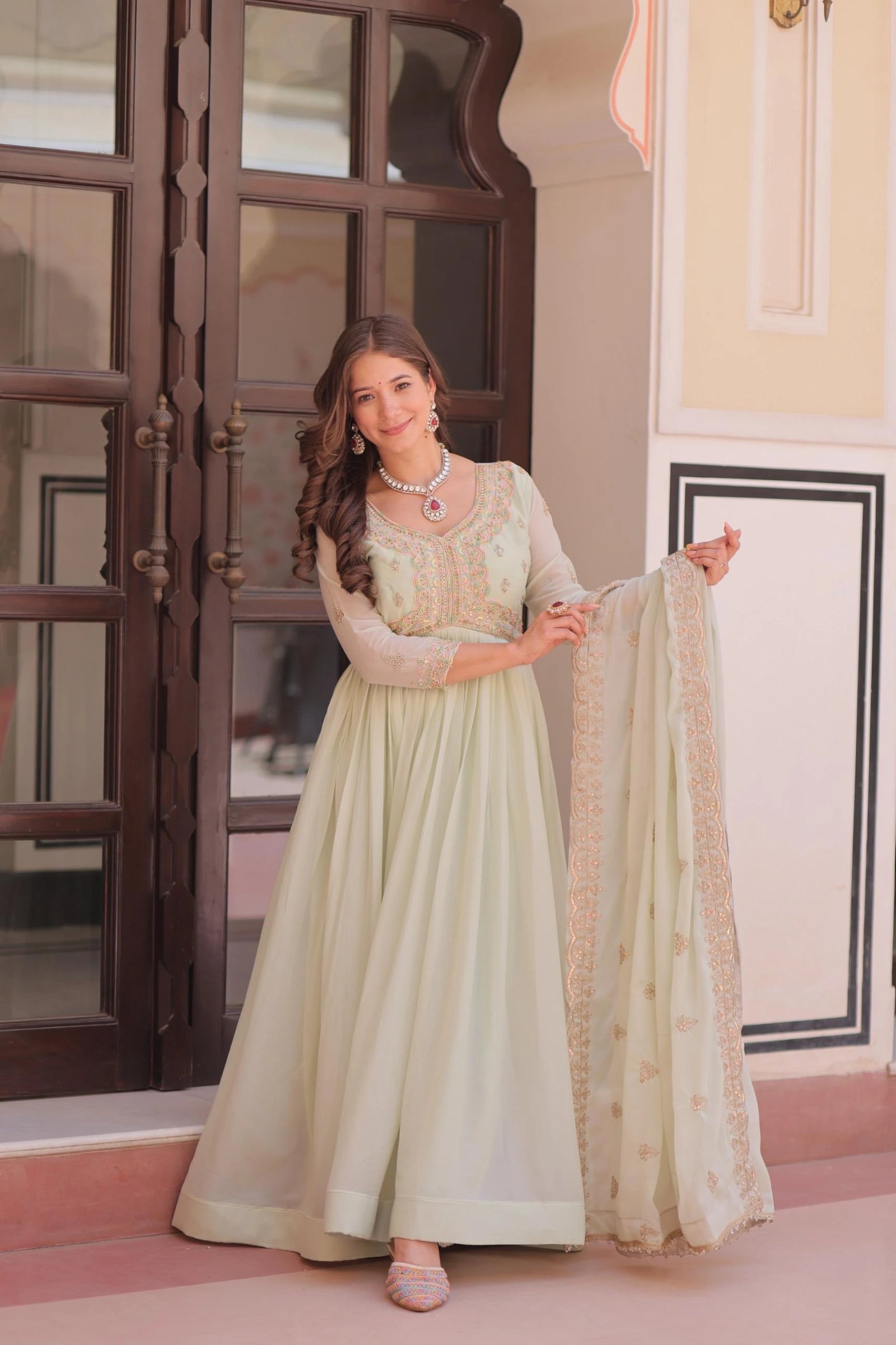 Woman in a light green traditional outfit holding a dupatta in an indoor setting.