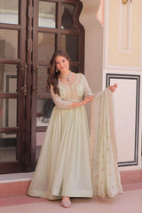 Woman in a light green traditional outfit holding a dupatta in an indoor setting.