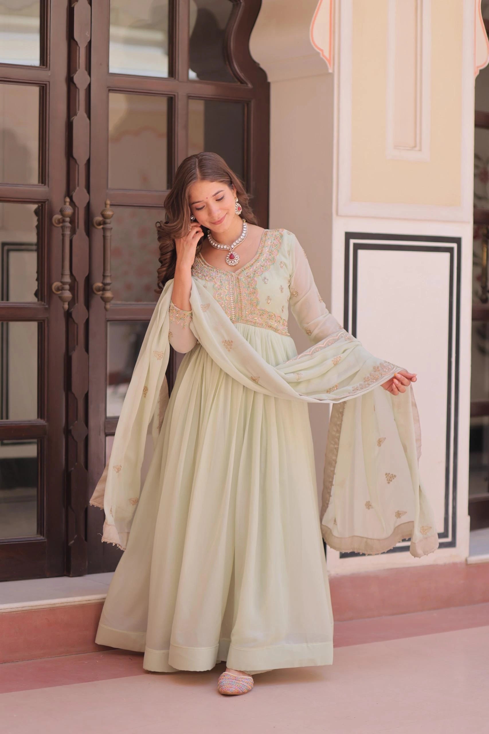 Woman in a light green traditional outfit standing in front of a decorative wall.