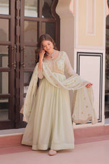 Woman in a light green traditional outfit standing in front of a decorative wall.