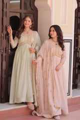 Two women in traditional outfits standing in front of a decorative door.