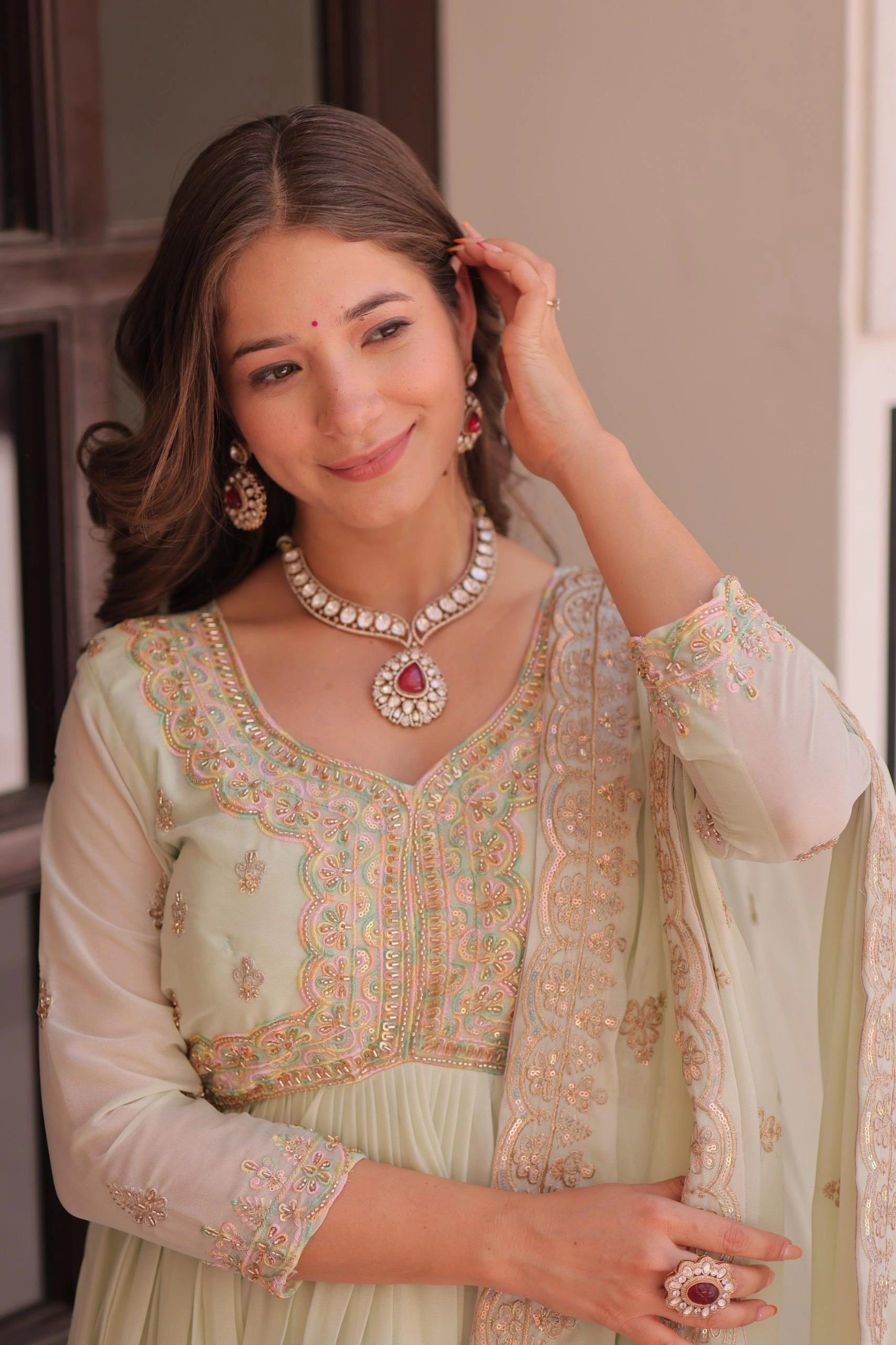 Woman wearing traditional light green embroidered outfit with jewelry indoors