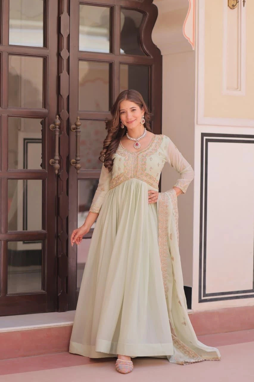 Woman in a light green traditional outfit standing in front of a decorative door.