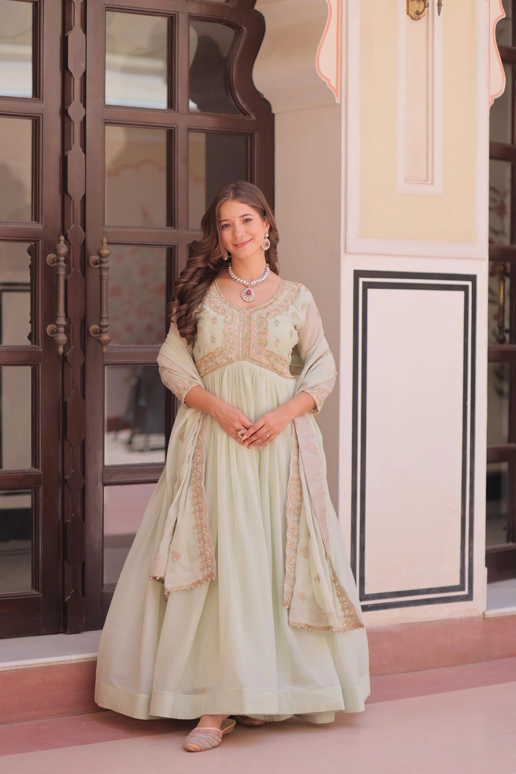 Woman in a light green traditional outfit standing in a decorative interior setting.