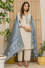 Woman wearing a white kurta with blue patterns, standing indoors with plants around.