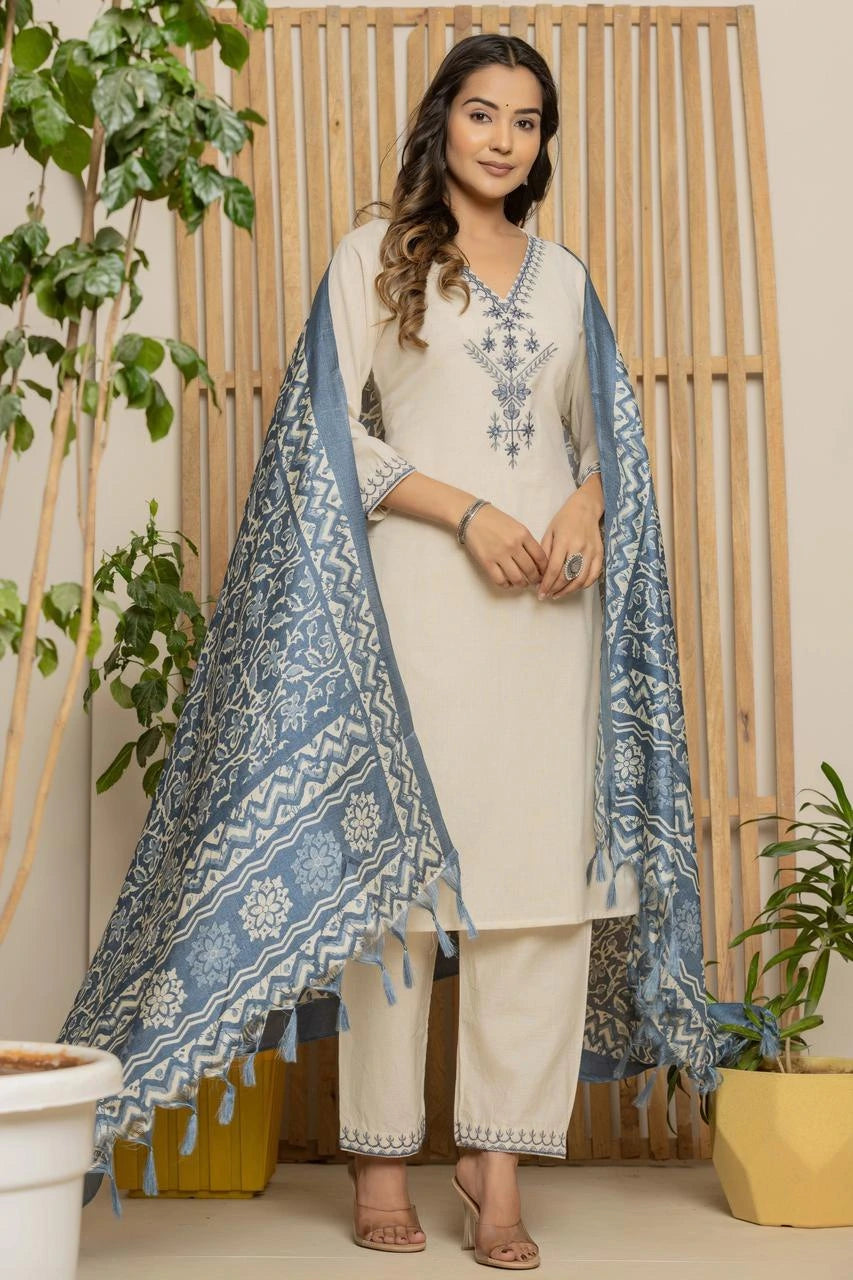 Woman wearing a white kurta with blue patterns, standing indoors with plants around.