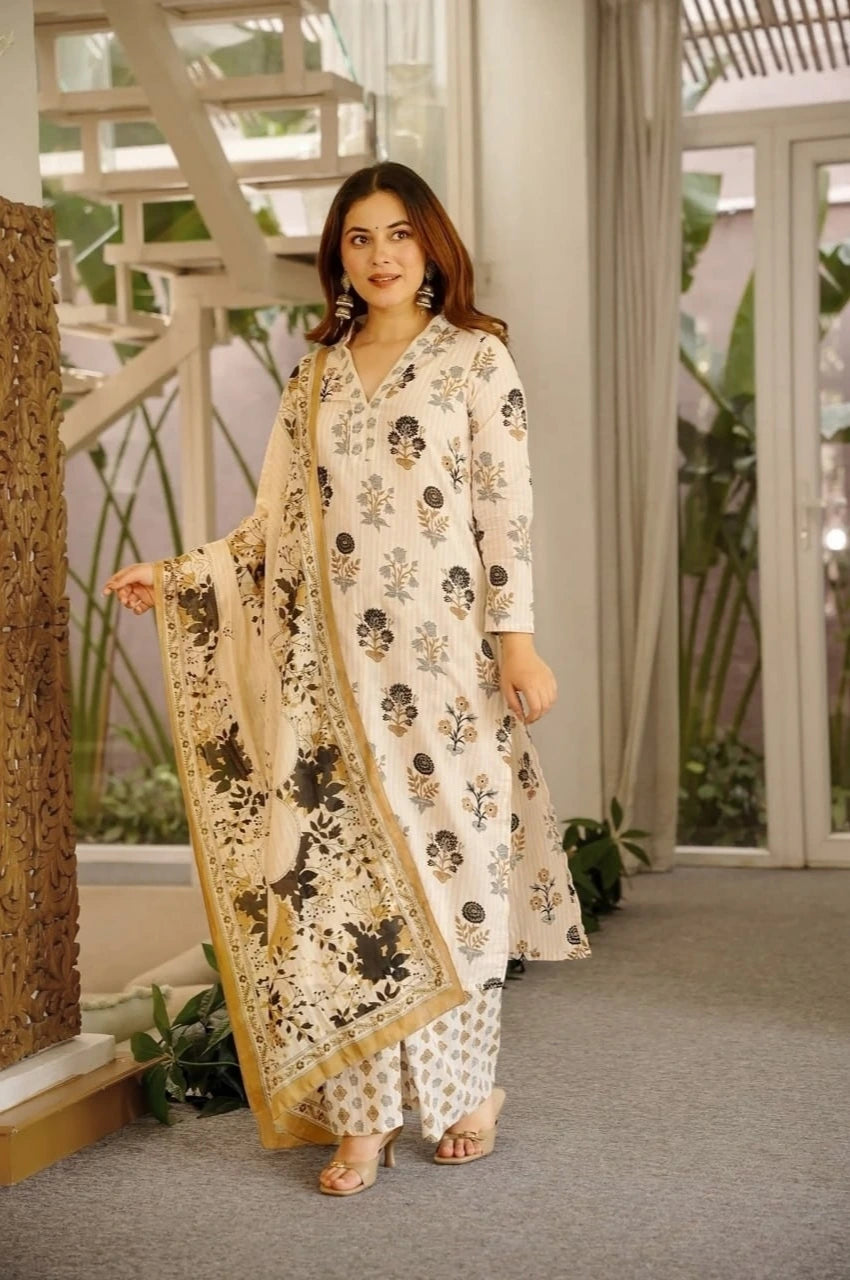 Woman in a floral outfit standing in an indoor setting with plants and a staircase.