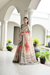 Woman in a floral saree standing in an elegant indoor setting with columns and plants.