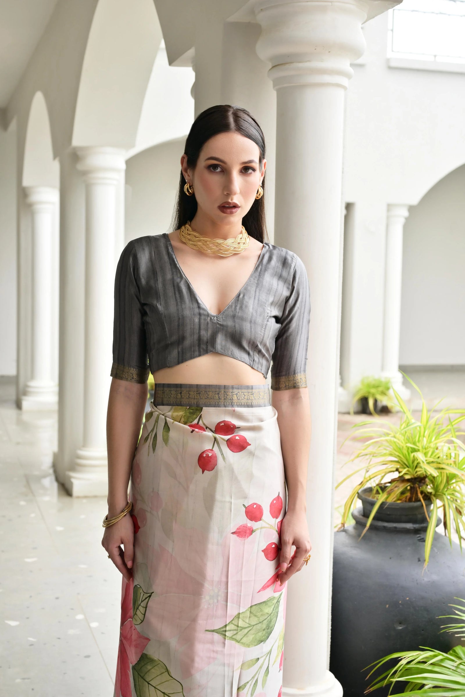 Woman in a traditional outfit with a floral skirt standing in a white architectural setting.