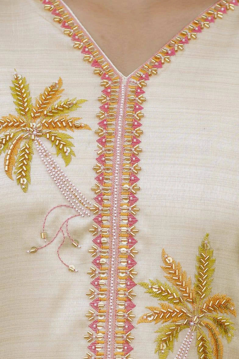 Close-up of embroidered fabric with palm tree designs and beadwork on a beige background