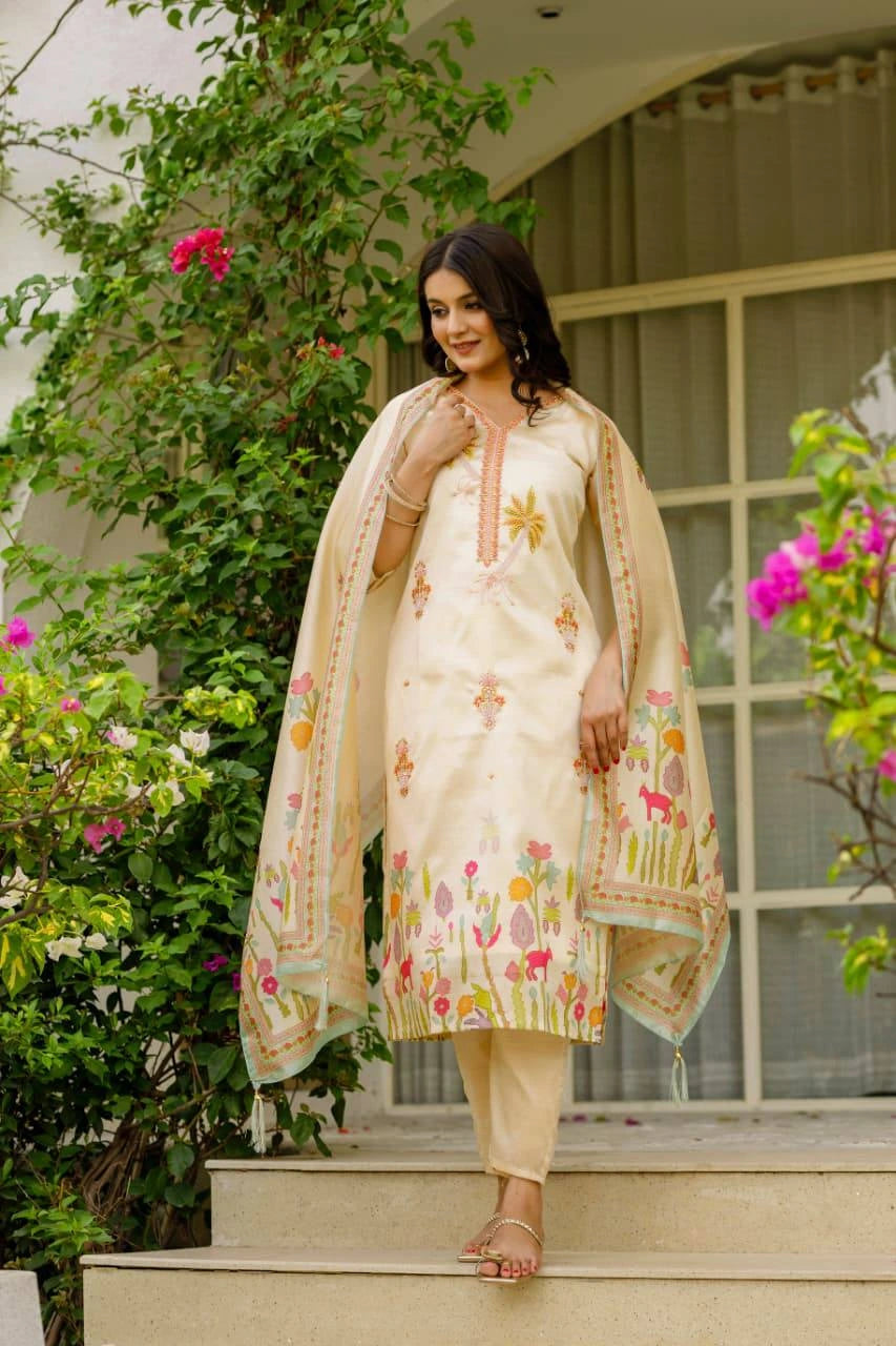 Woman in a cream-colored traditional outfit with floral patterns standing outdoors.