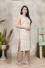 Woman wearing a patterned outfit standing against a textured wall with a plant and chair in the background.