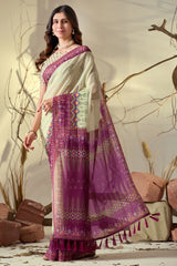 Woman wearing a traditional saree with a purple and white design, standing against a natural background.