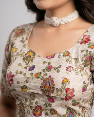 Close-up of a person wearing a floral embroidered top with a pearl necklace against a neutral background